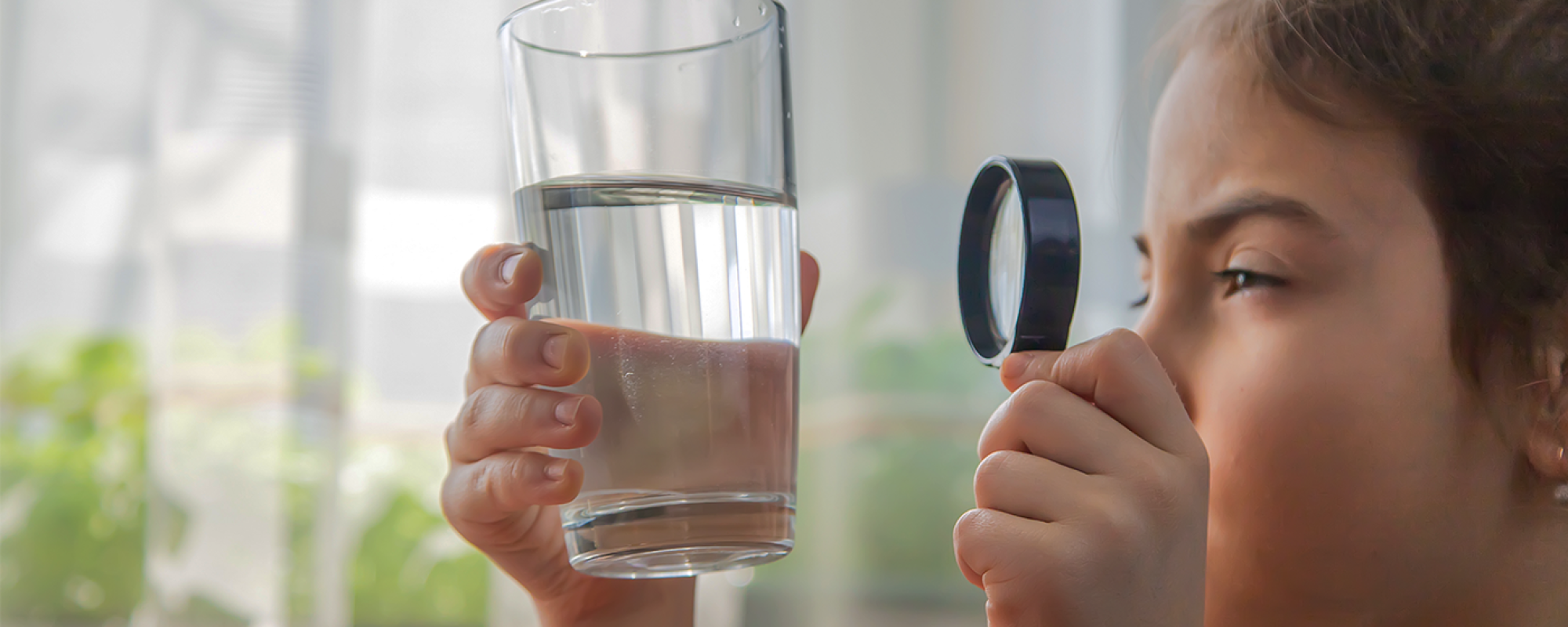 Home page photo of child examining a glass of water with magnifying glass.